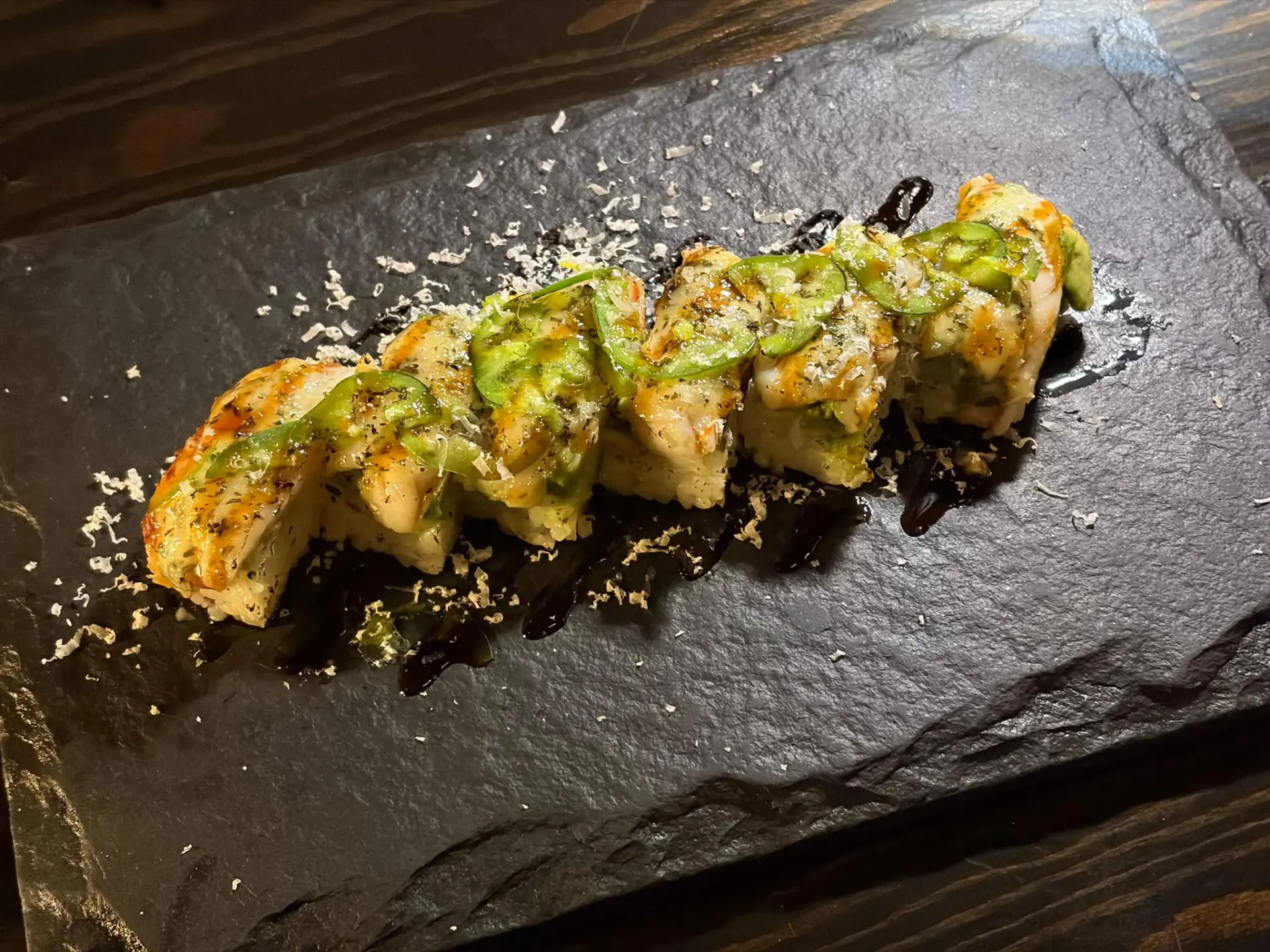 Pressed sushi topped with jalapeño and furikake on black slate